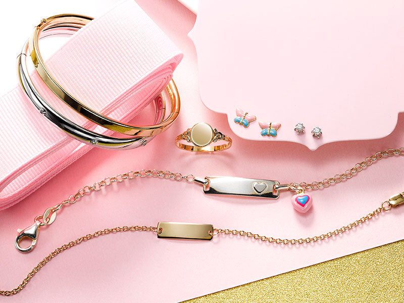 Children's bangles, ID bracelets, a signet ring and tiny stud earrings on pink
